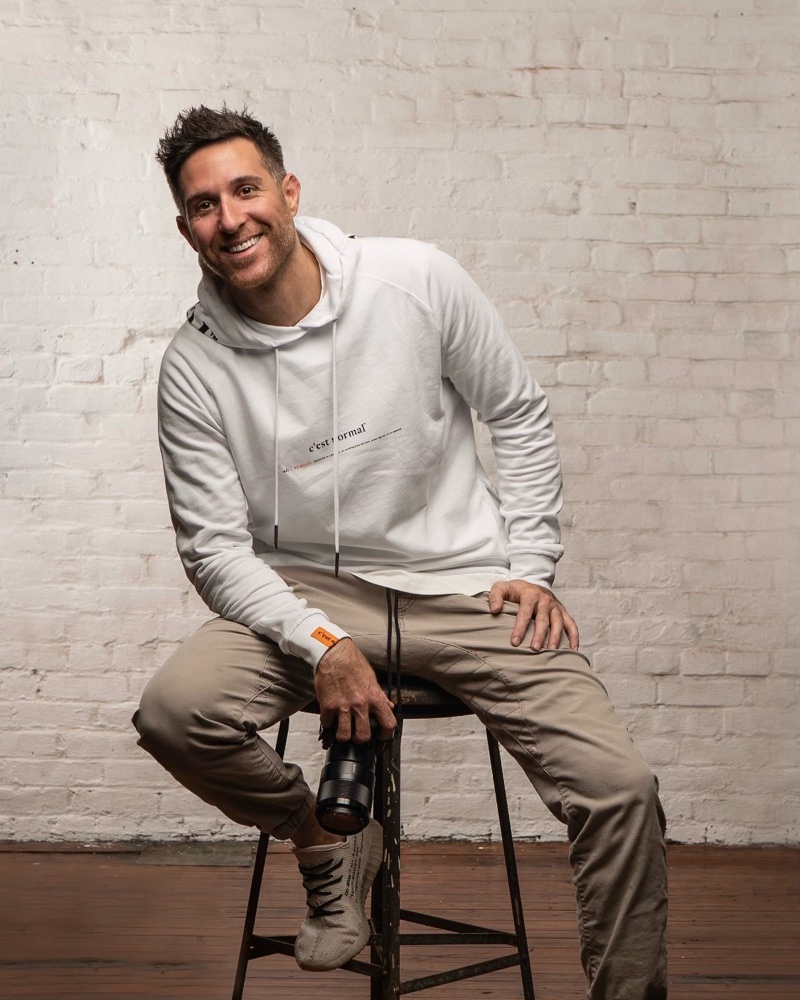 Ryan Fredericks, who made Snapshots, sitting on a stool and smiling, a camera lens in his hand.